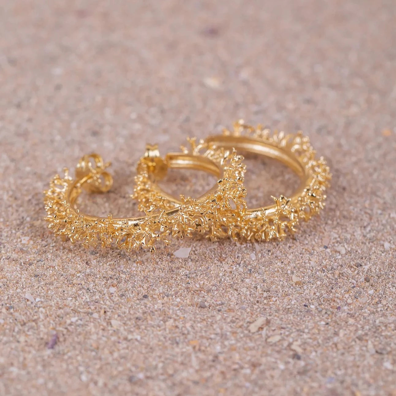 Aros de Coralina grandes bañados en Oro uno encima del otro posados sobre arena, detalles en macro.