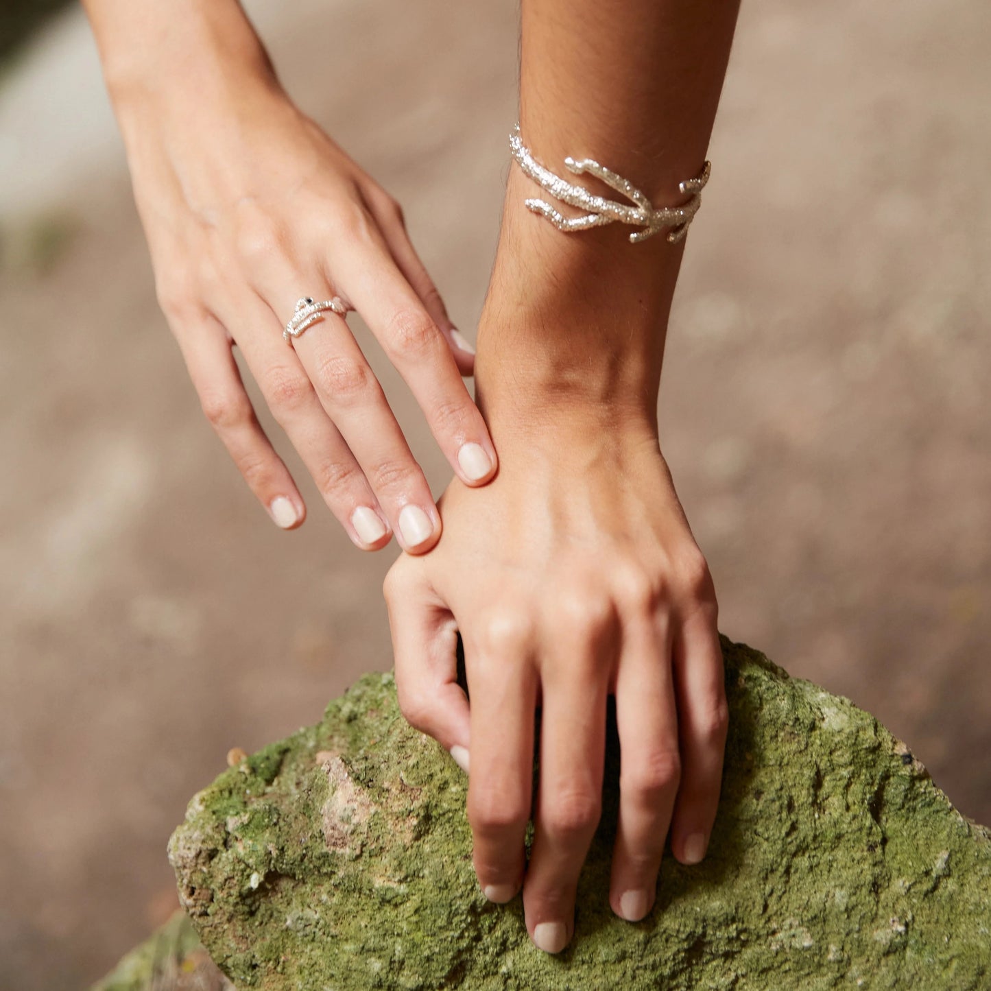 Detalles de mano de modelo apoyada en una roca verde luciendo el Brazalete de Eunicella en Plata.