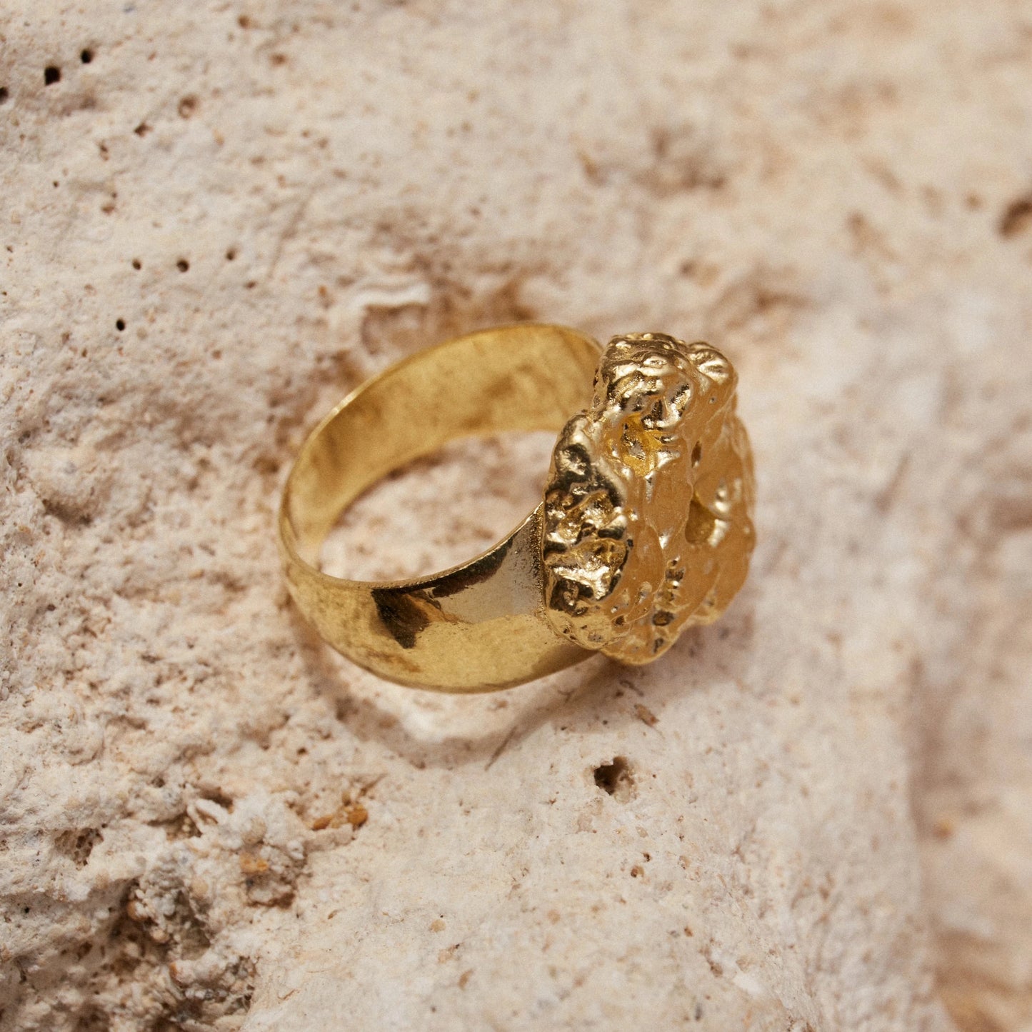 Detalles en Macro del Anillo de Esponja bañado en Oro sobre roca beige.