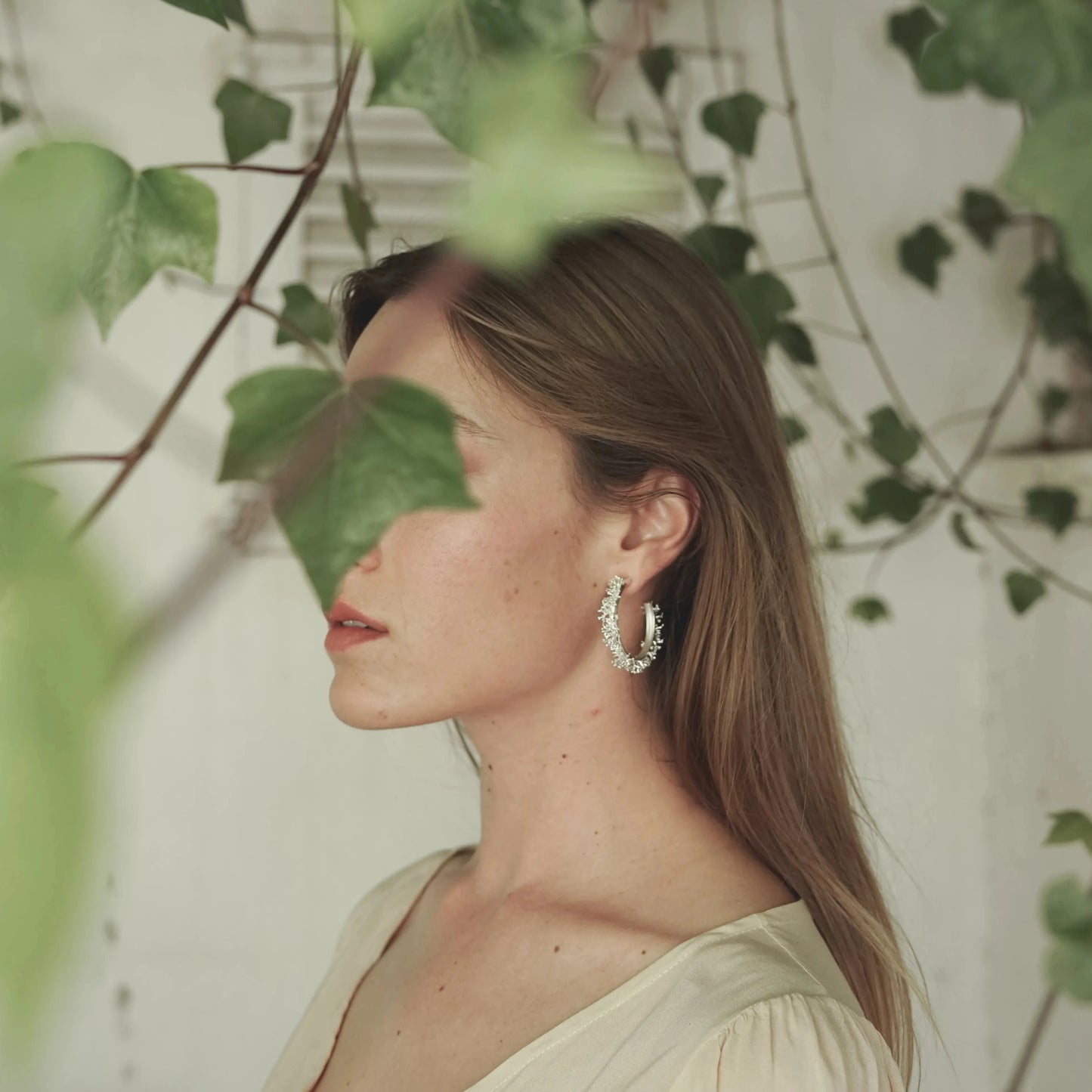 Modelo de perfil luciendo los Aros de Coralina en Plata con hojas verdes tapándole sutilmente la cara