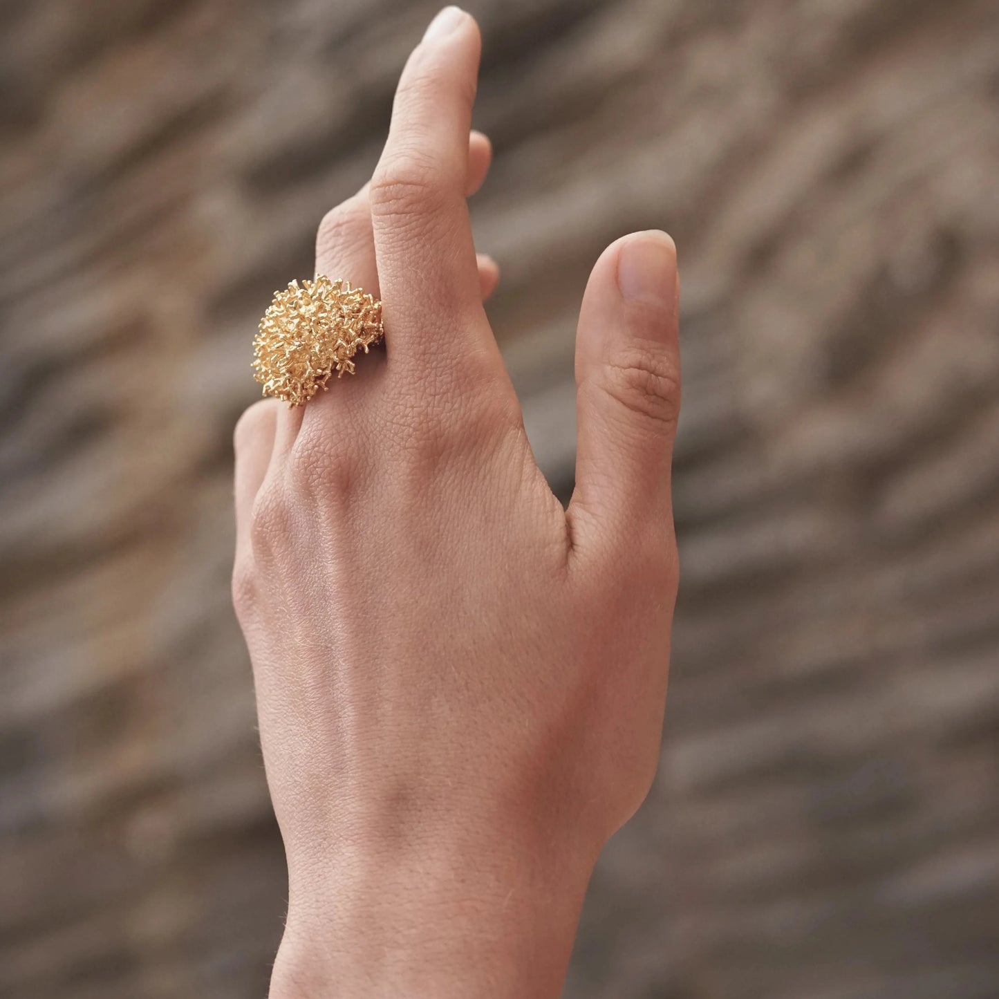 Mano de modelo luciendo el Anillo grande de Coralina bañado en Oro.