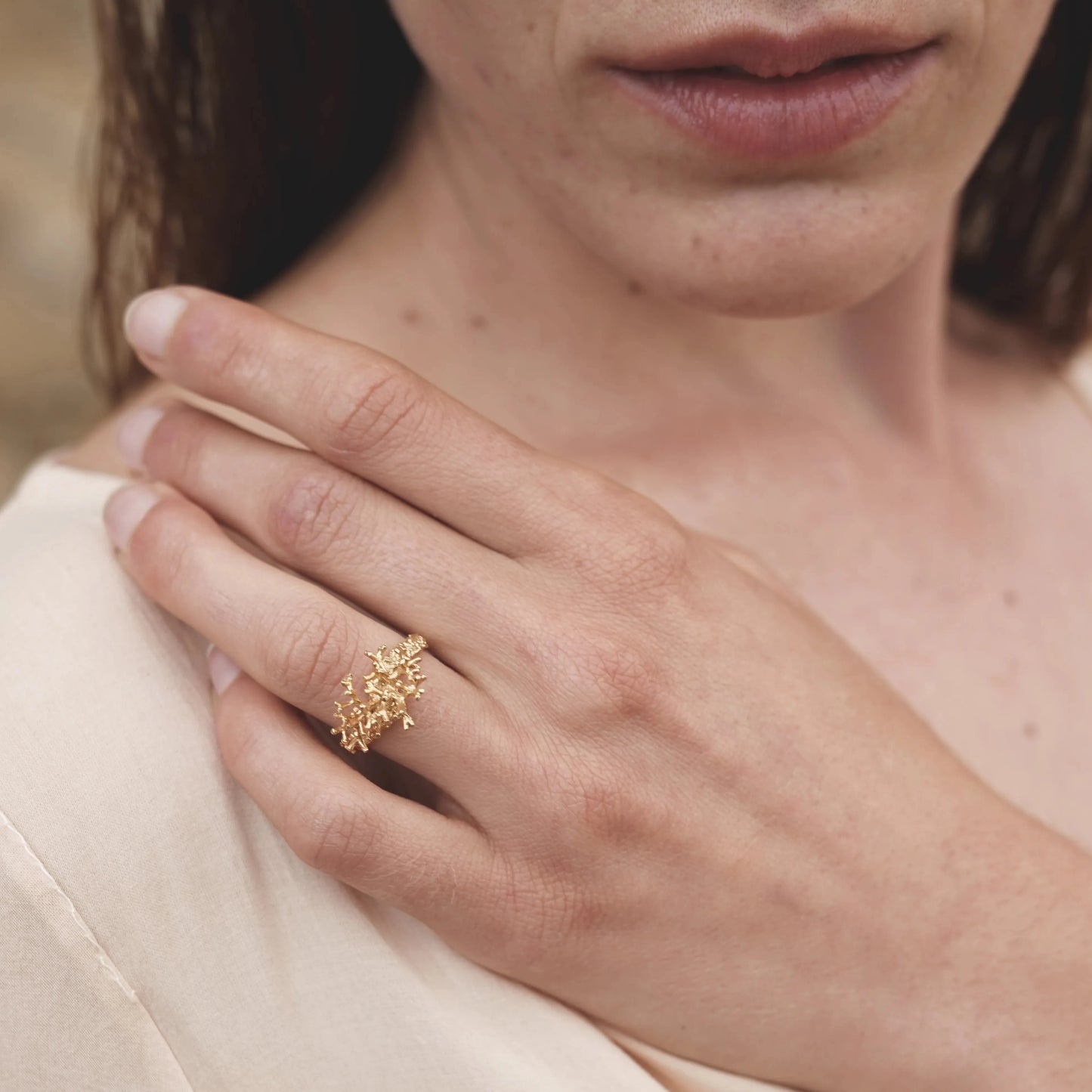 Modelo morena con mano en el hombro luciendo el Anillo de Coralina pequeño en Oro.