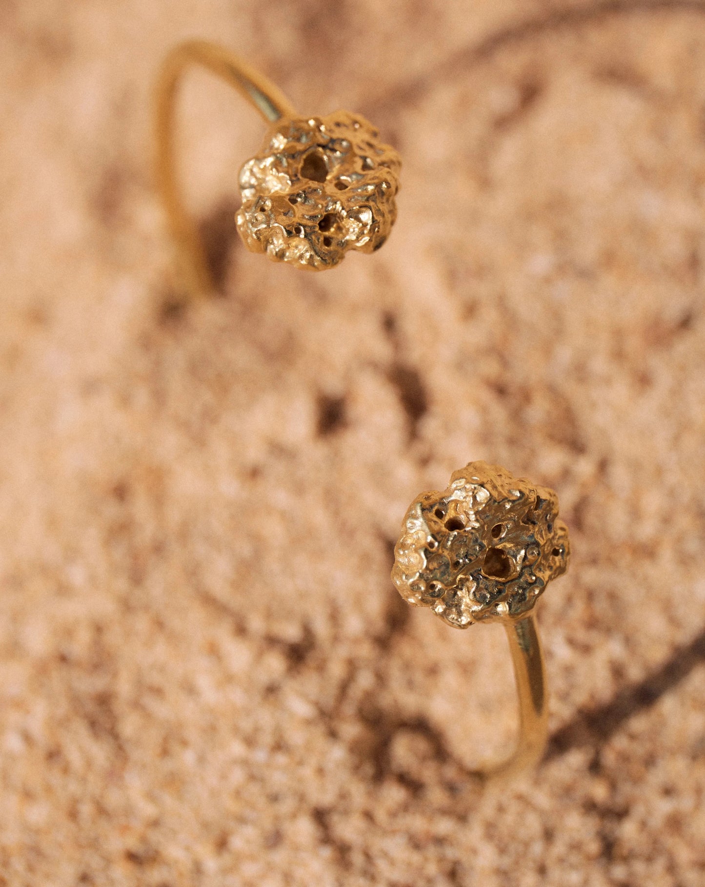 Detalles en macro del Brazalete de Esponja bañado en Oro parcialmente hundido en la arena.