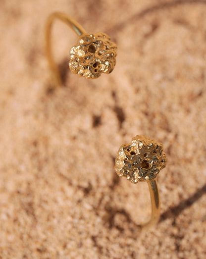 Detalles en macro del Brazalete de Esponja bañado en Oro parcialmente hundido en la arena.