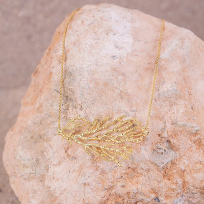 Detalles en macro del colgante lateral de Gorgonia bañado en Oro sobre roca beige.