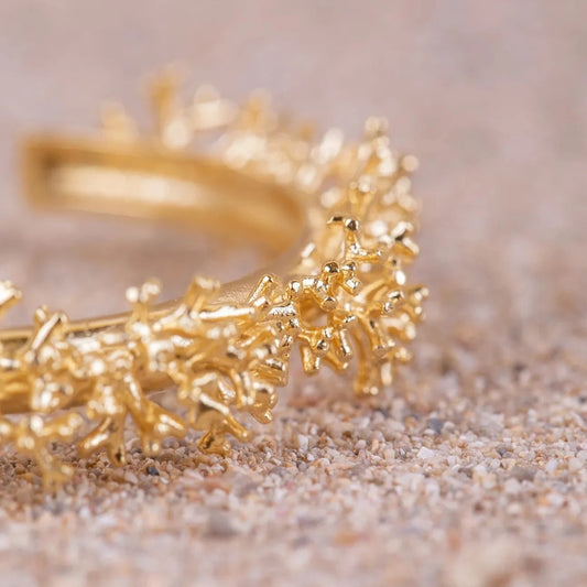 Detalles en macro de los Aros de Coralina bañados en Oro sobre arena.