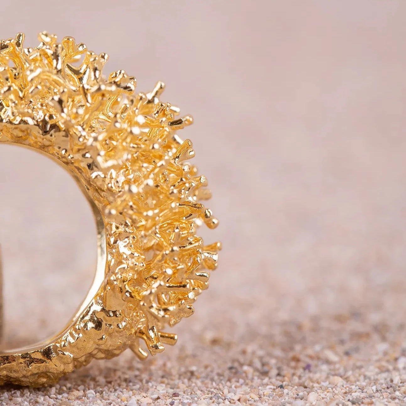 Detalles en macro del Anillo Coralina bañado en Oro posado de perfil sobre arena.