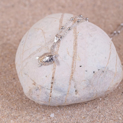 Colgante Cayume (Tortuga) en Plata sobre roca blanca y fondo arenoso.