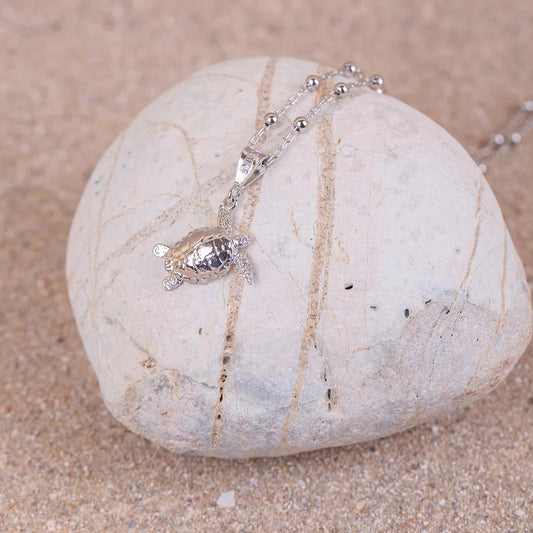 Colgante Cayume (Tortuga) en Plata sobre roca blanca y fondo arenoso.