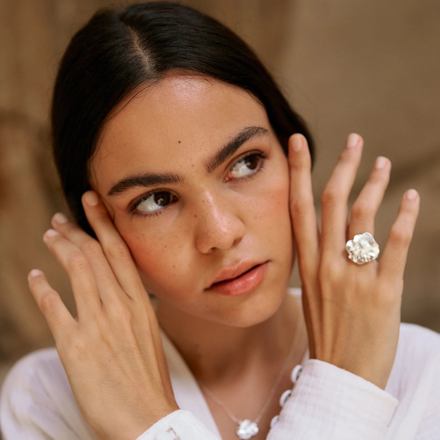 Modelo morena cruzando las manos en su cara luciendo el Anillo de Pétalo en Plata.