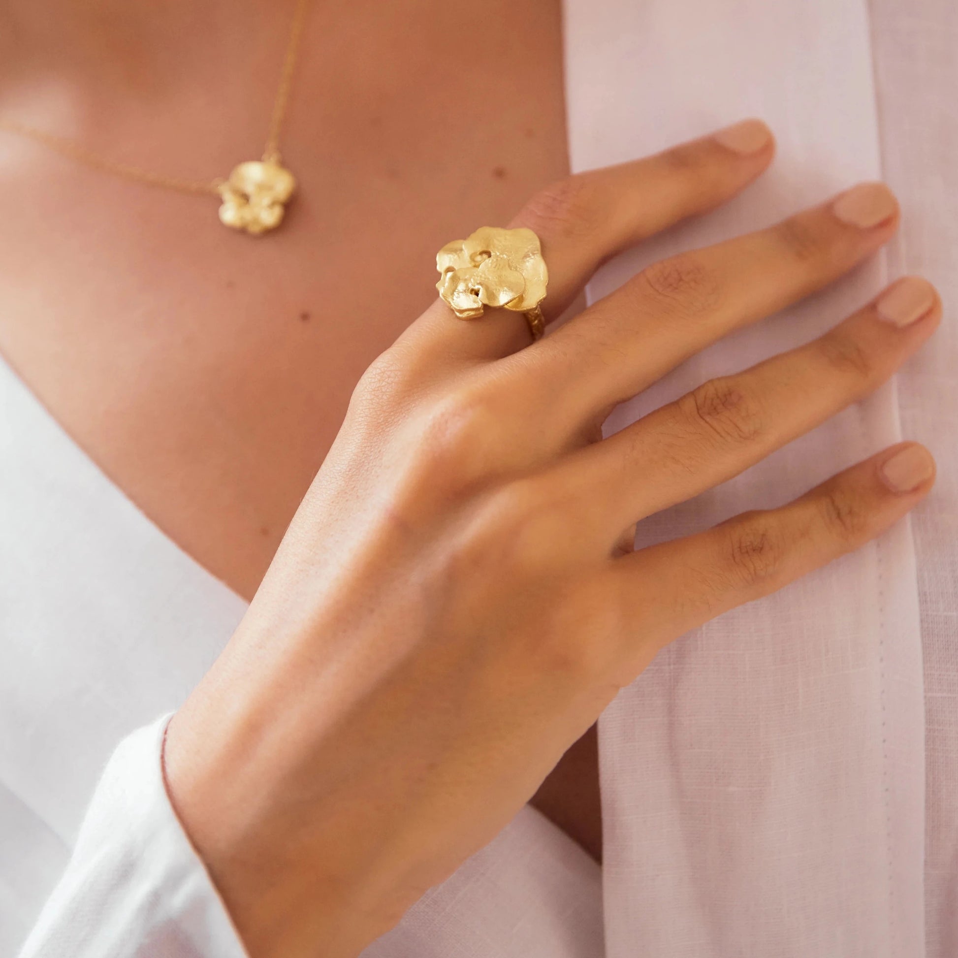 Mano de una modelo con mano en el pecho luciendo el Anillo de Pétalo en Oro.