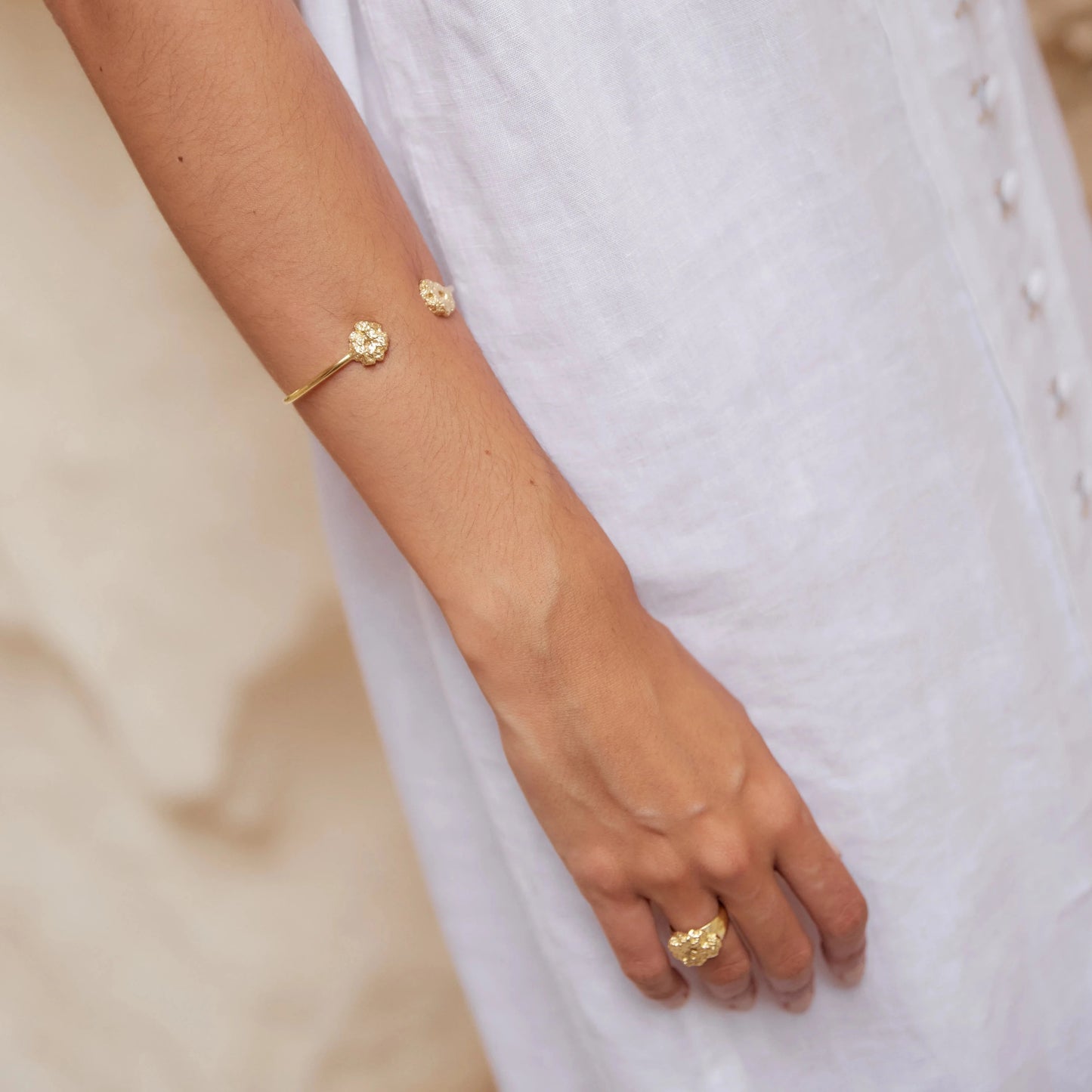 Modelo luciendo el brazalete de Esponja bañado en Oro con traje de lino blanco con fondo arenoso.