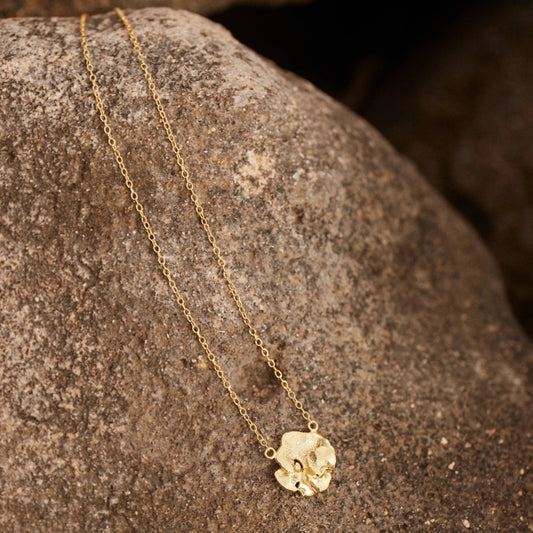 Colgante Solitario bañado en Oro de la colección Pétalo, apoyado sobre roca arenosa.